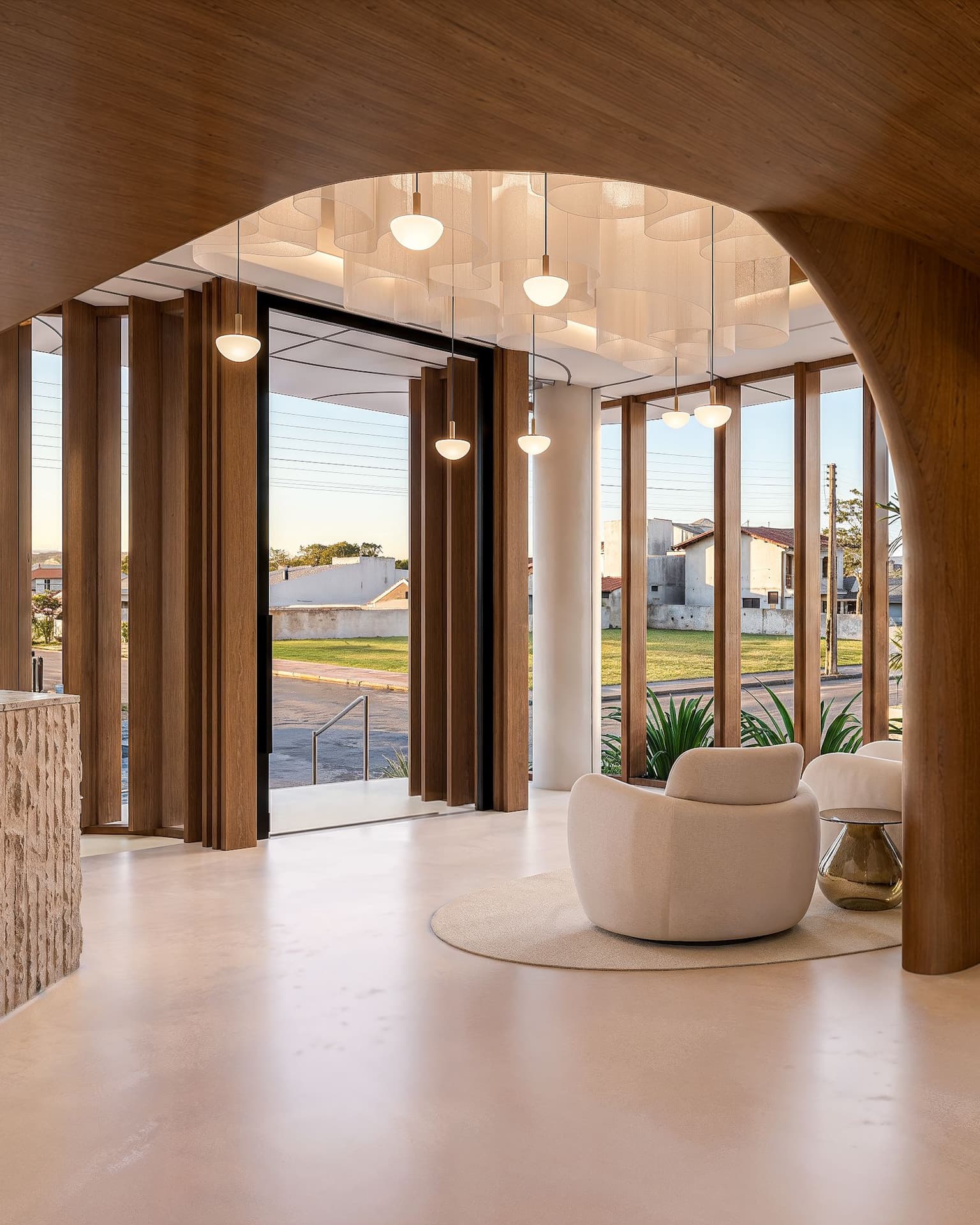 Render do hall de entrada no térreo, com arco revestido de madeira, poltronas claras e portas de vidro voltadas para a rua
